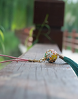 Zen Aroma Flora Bloom Sachet Pendant with golden filigree cage, enamel floral design, and green silky tassel — crafted to hold up to two aroma pellets, blending fragrance with ornamental charm.