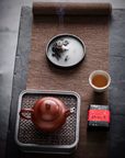 Tea set with a red teapot, white cup, and tea leaves on a textured surface.