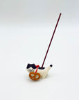 Cat and pretzel ceramic incense holder shown in use with a vertical incense stick inserted.