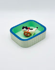 Cat and pretzel incense holder placed inside a mint-green Purrfect Ash Tub.