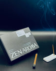 Zen Aroma “Midnight Sampler” box with a burning incense stick and gentle smoke rising in the background, styled on a dark surface to evoke a calm and elegant mood.
