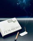 Zen Aroma “Serenity Sampler” incense set displayed with a burning incense stick releasing gentle smoke beside the box and holder, captured on a dark background to evoke calm and serenity.