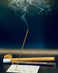 Lit Zen Aroma incense stick releasing gentle smoke, displayed with glass and cardboard packaging on a dark background — a serene and elegant home fragrance scene.