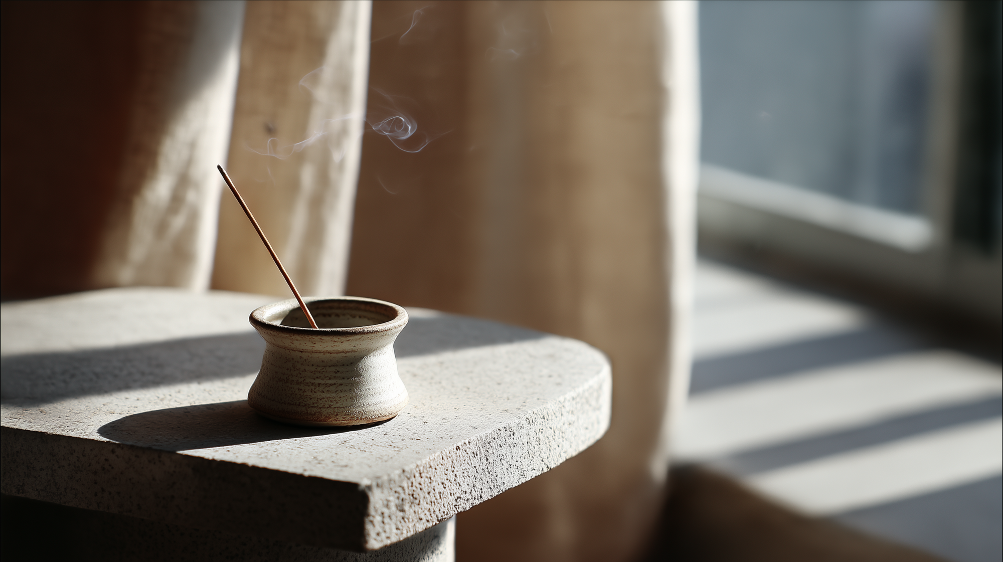 A single incense stick burning in a small ceramic holder by a sunlit window, with gentle smoke curling in the calm morning light.