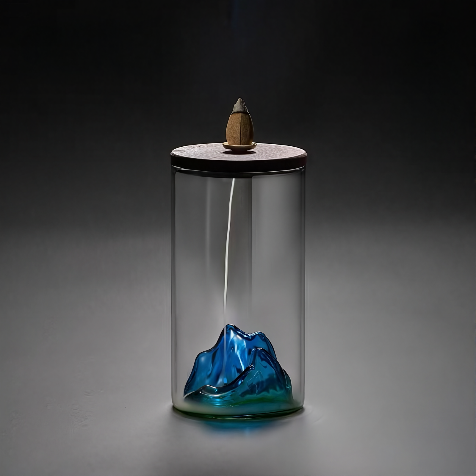 Glass container with a blue mountain design and a small wooden figure on a dark background