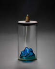 Glass container with a blue mountain design and a small wooden figure on a dark background
