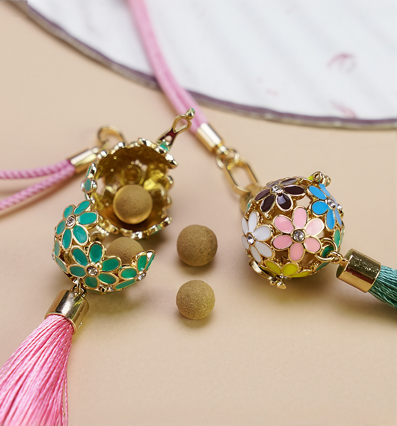 Zen Aroma Flora Bloom Sachet Pendants with golden floral filigree cages and silky tassels, shown on a beige surface. One pendant is open, displaying aroma pellets inside.