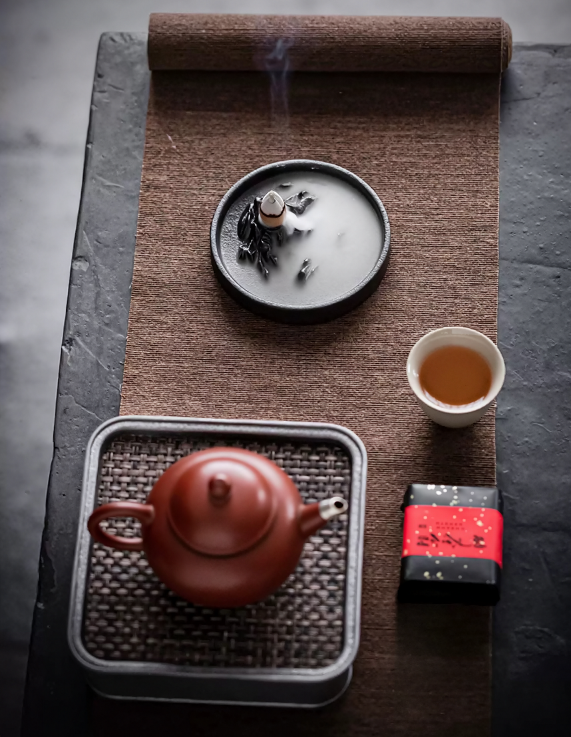 Tea set with a red teapot, white cup, and tea leaves on a textured surface.