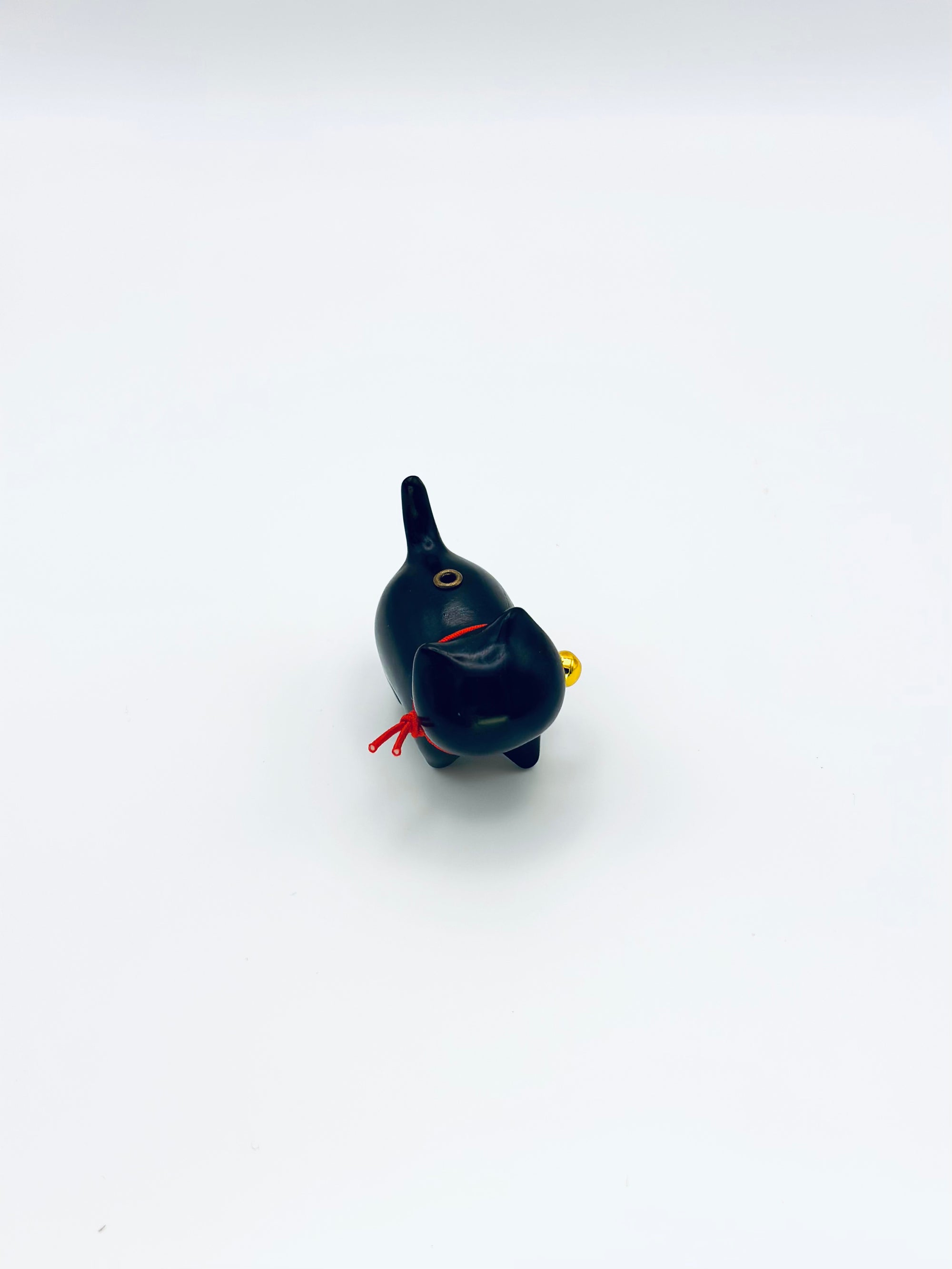 top view of Cat & Bell incense holder with a red string and gold bell on a minimal white backdrop.