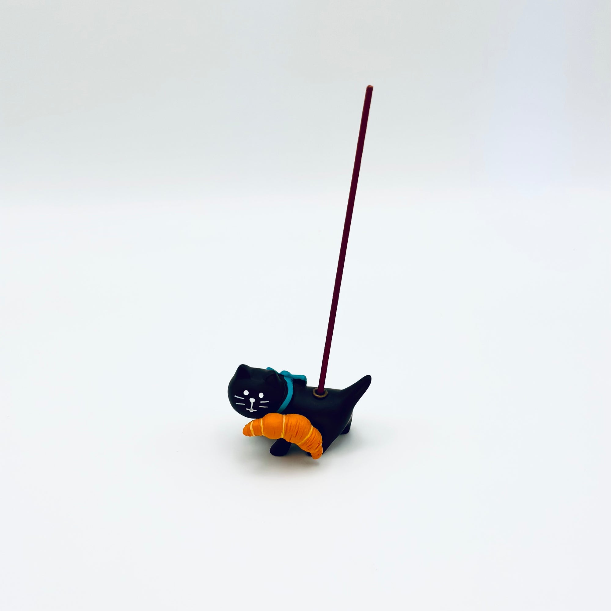 Cat and croissant resin incense holder shown in use with an upright burning incense stick.