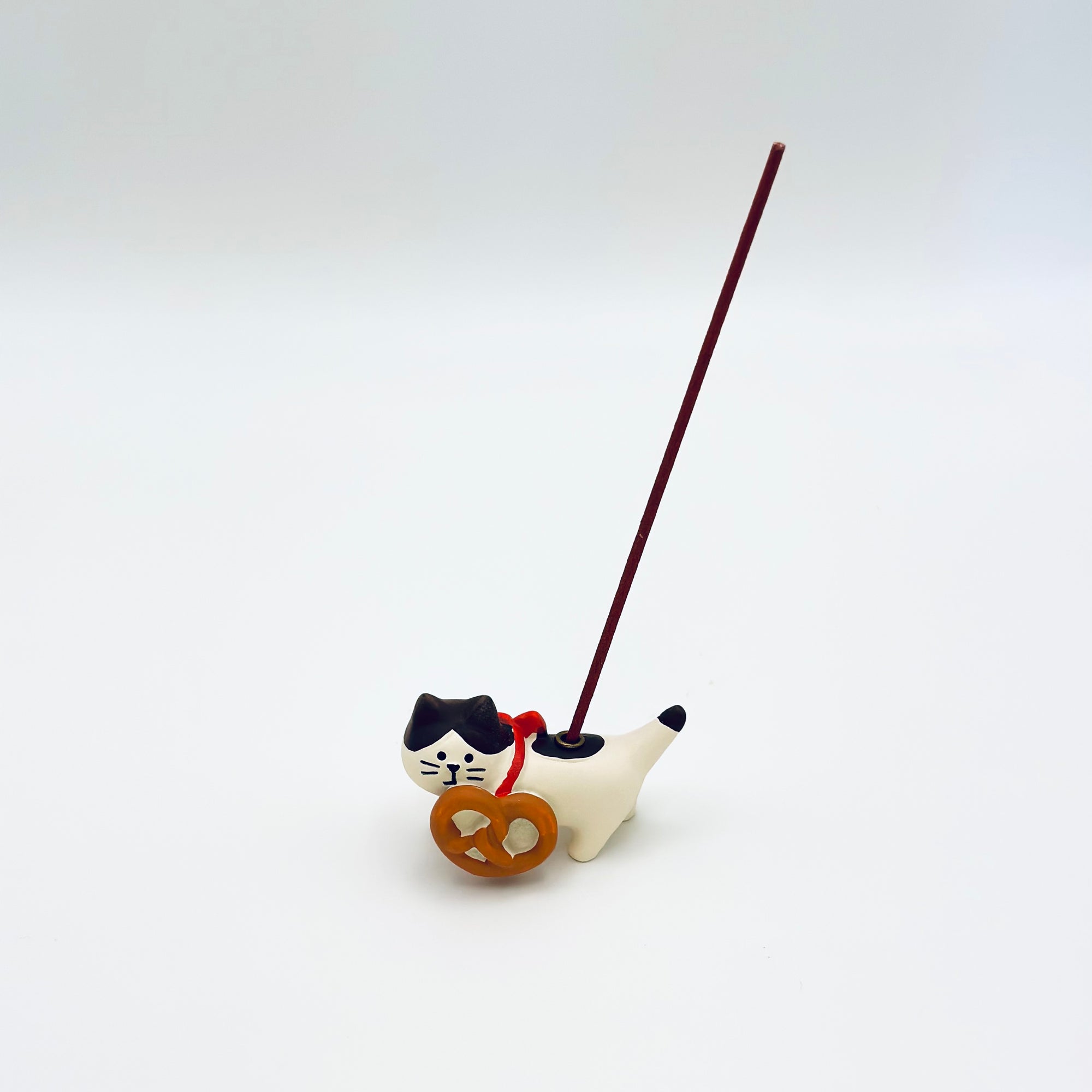 Cat and pretzel ceramic incense holder shown in use with a vertical incense stick inserted.