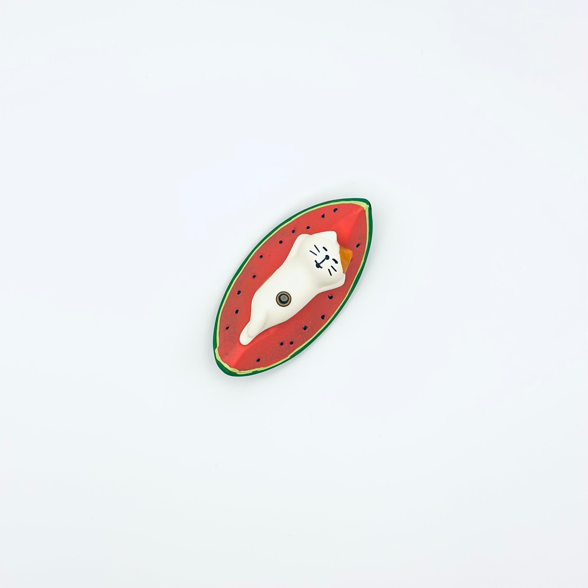 Top view of a ceramic cat lying on a watermelon slice incense holder against a white backdrop.