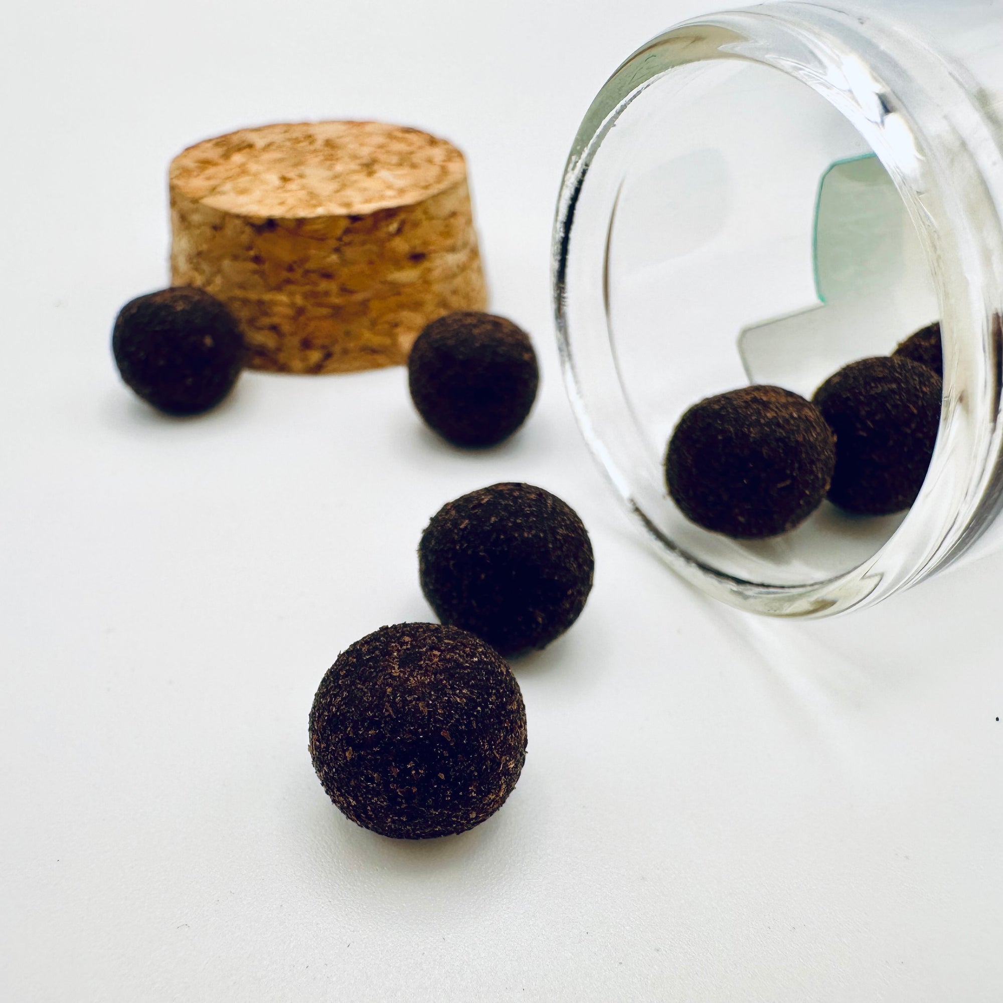 Close-up of Zen Aroma aroma pellets spilling from a glass jar with a cork lid, showcasing their natural texture and rich earthy color on a light background.