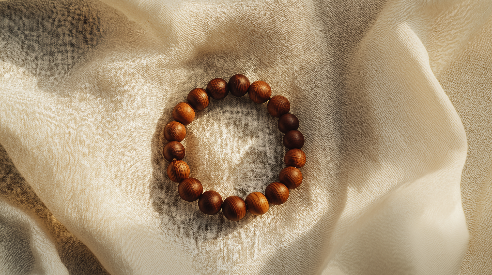 Hainan Huanghuali wood bead bracelet on soft beige fabric, minimalist zen-inspired flatlay with warm natural light