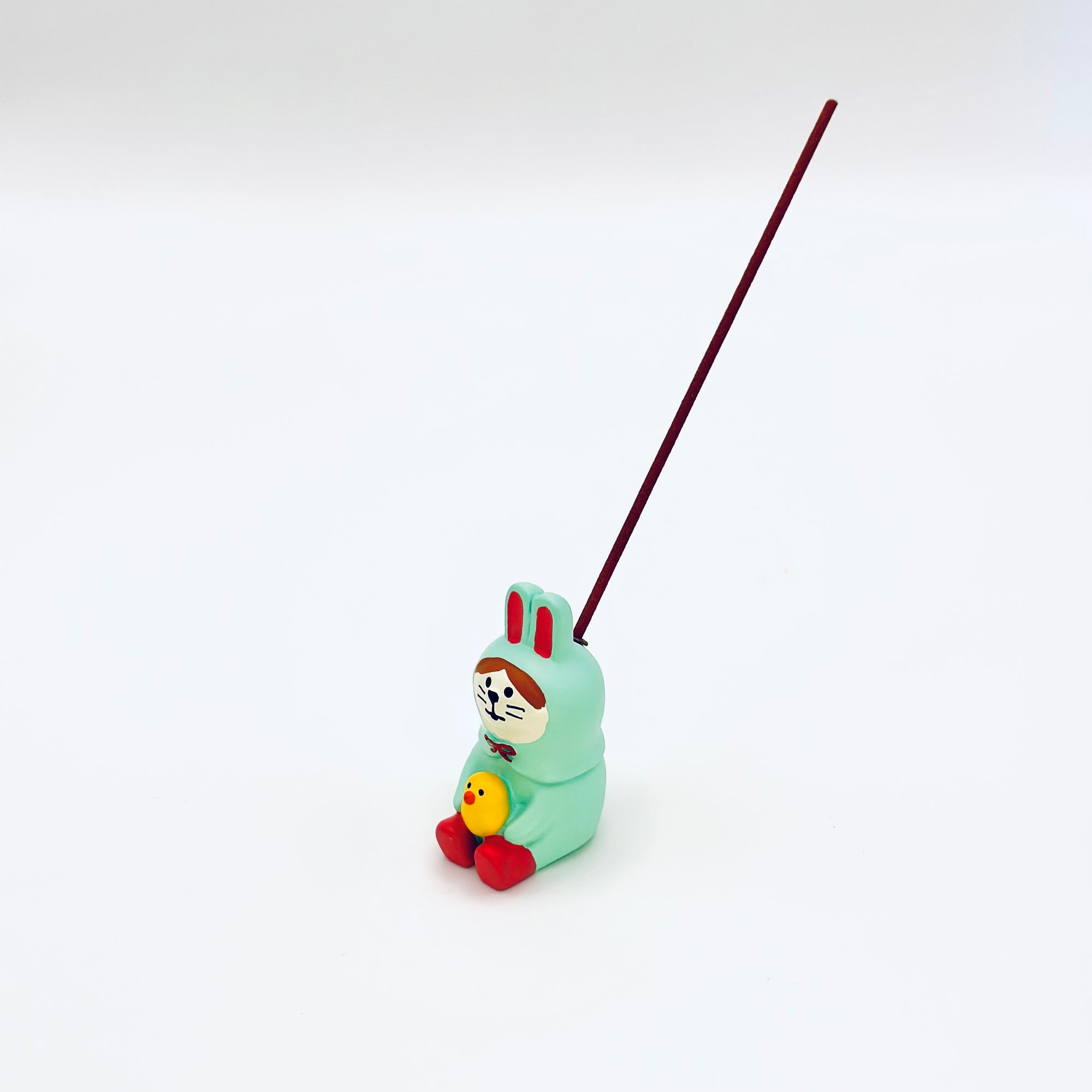 The bunny-and-chick resin incense holder in use, securely holding a burning incense stick against a minimalist white backdrop.