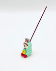 The bunny-and-chick resin incense holder in use, securely holding a burning incense stick against a minimalist white backdrop.