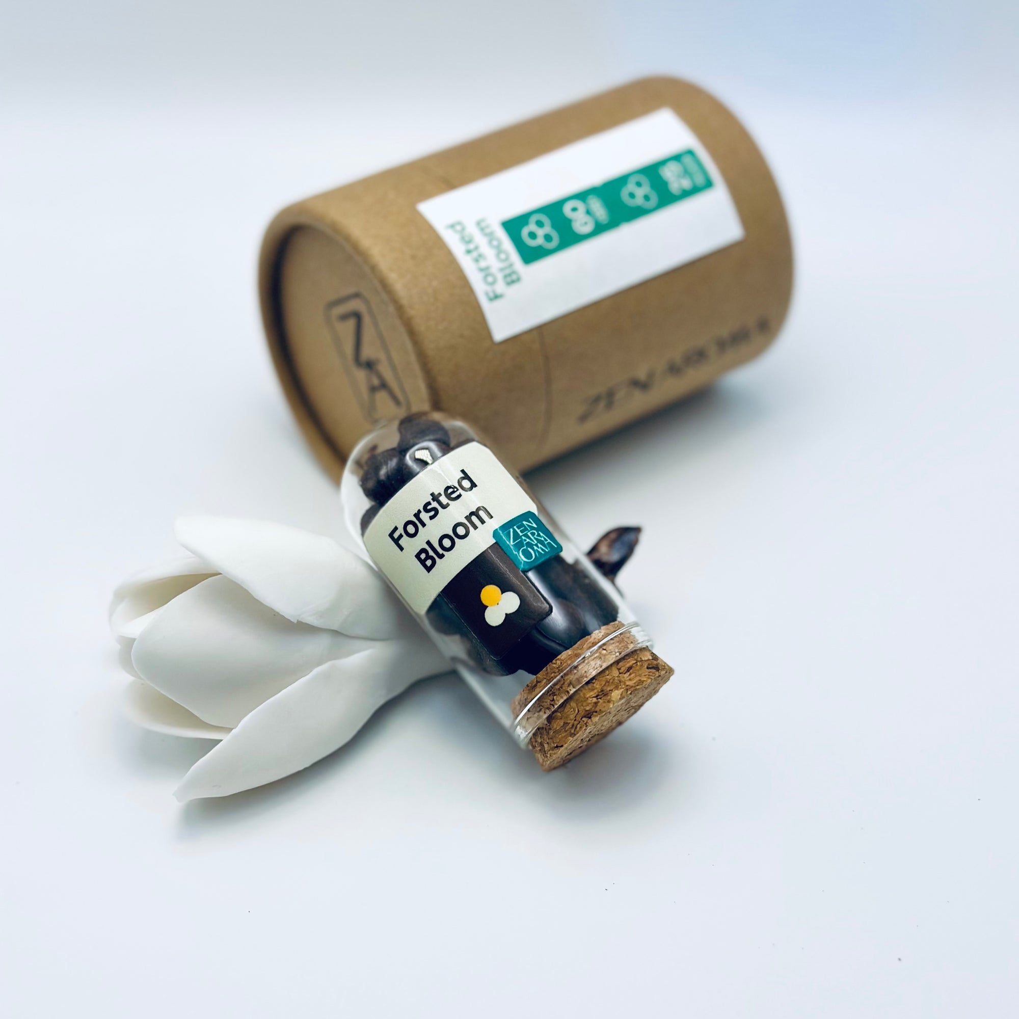Zen Aroma Frosted Bloom aroma pellets in a glass jar with cork lid, displayed with a kraft paper tube and white flower petals on a light background.