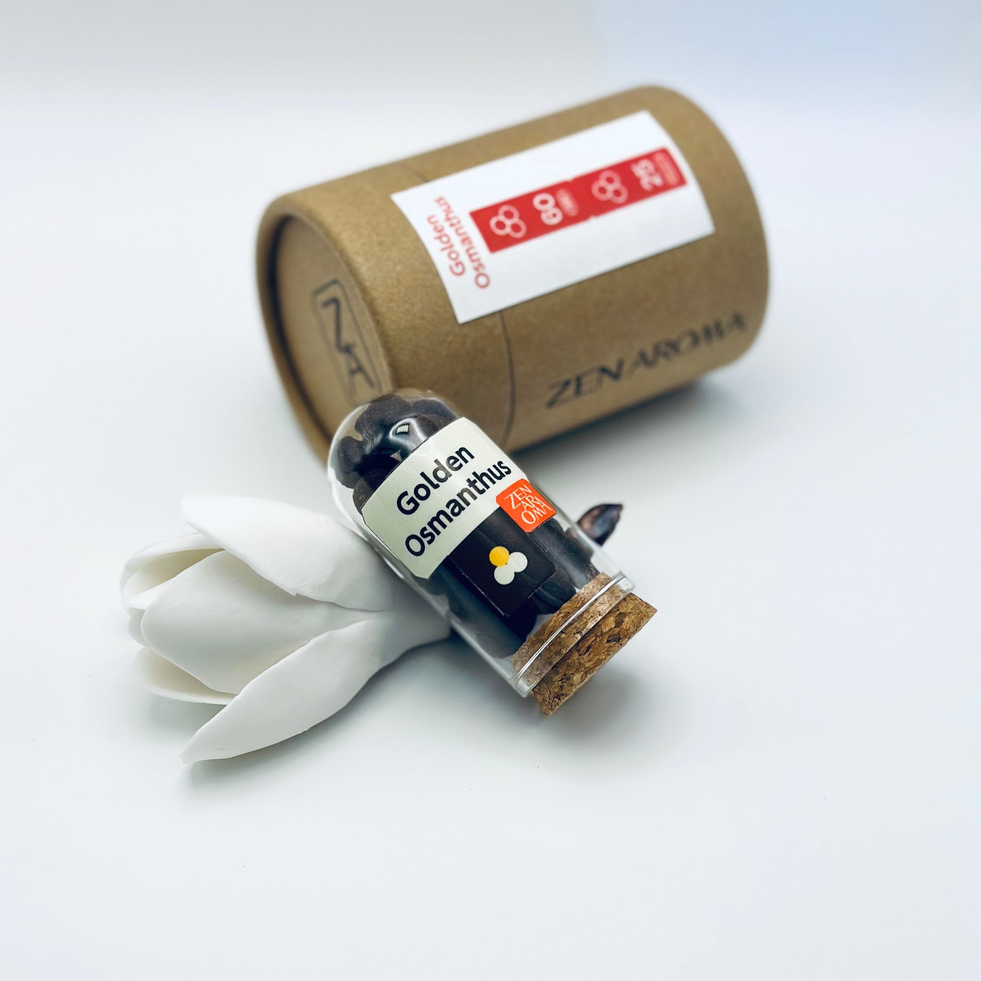 Zen Aroma Golden Osmanthus aroma pellets in a glass jar with cork lid, displayed with a kraft paper tube and white flower petals on a light background.