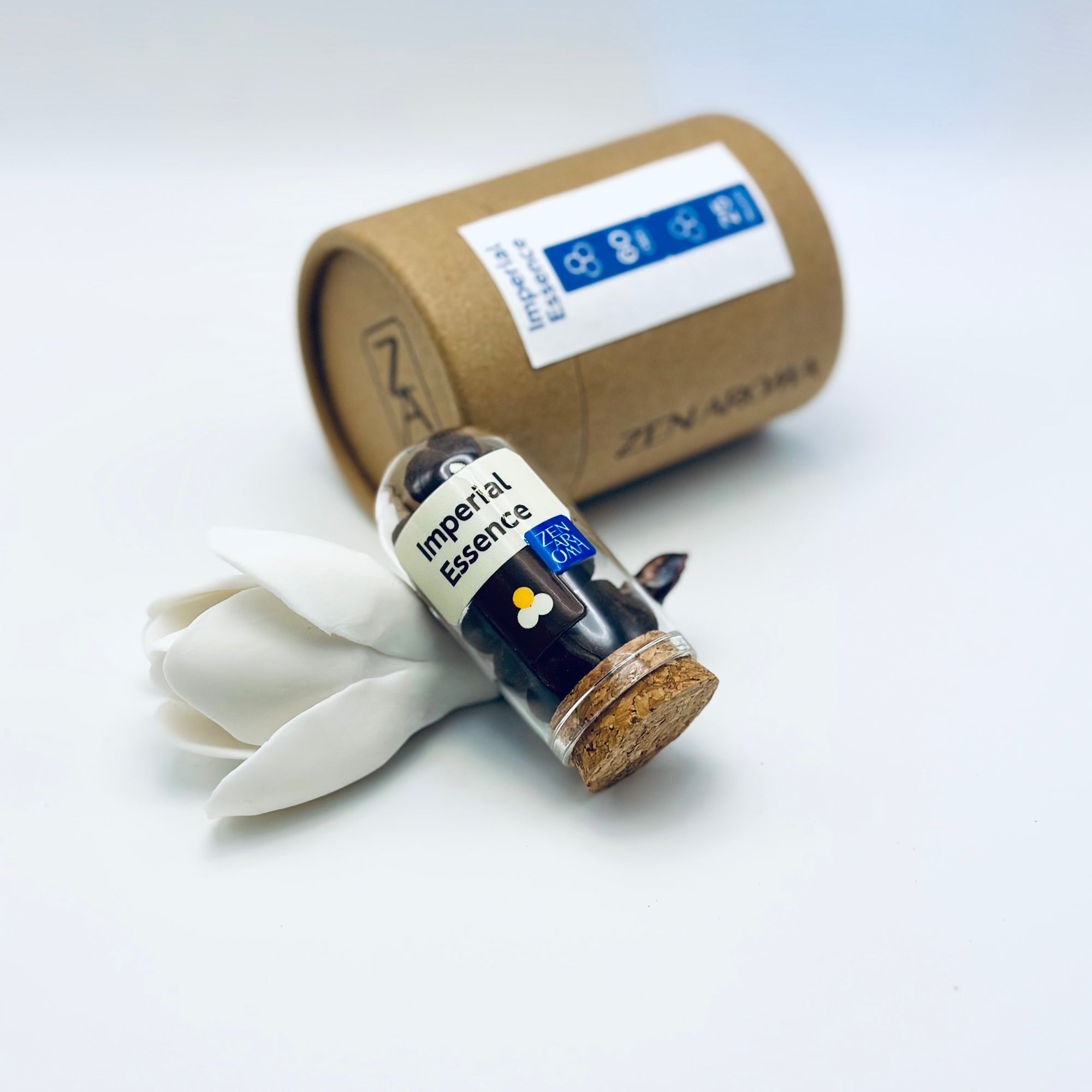 Zen Aroma Imperial Essence aroma pellets in a glass jar with cork lid, displayed with a kraft paper tube and white flower petals on a light background.