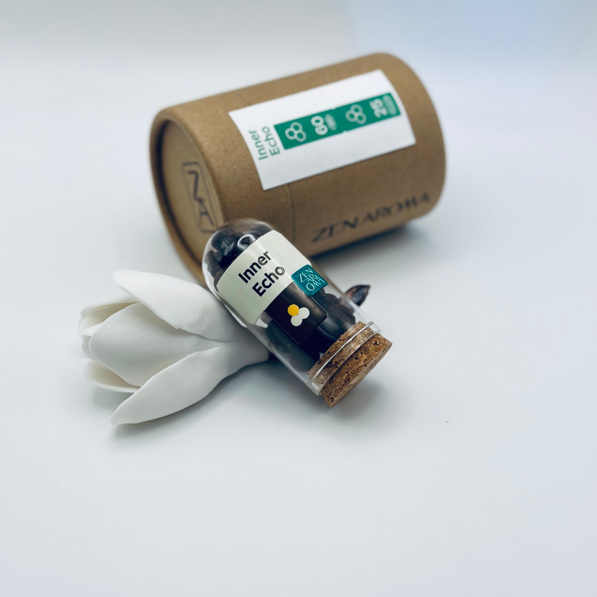 Zen Aroma Inner Echo aroma pellets in a glass jar with cork lid, displayed with a kraft paper tube and white flower petals on a light background.