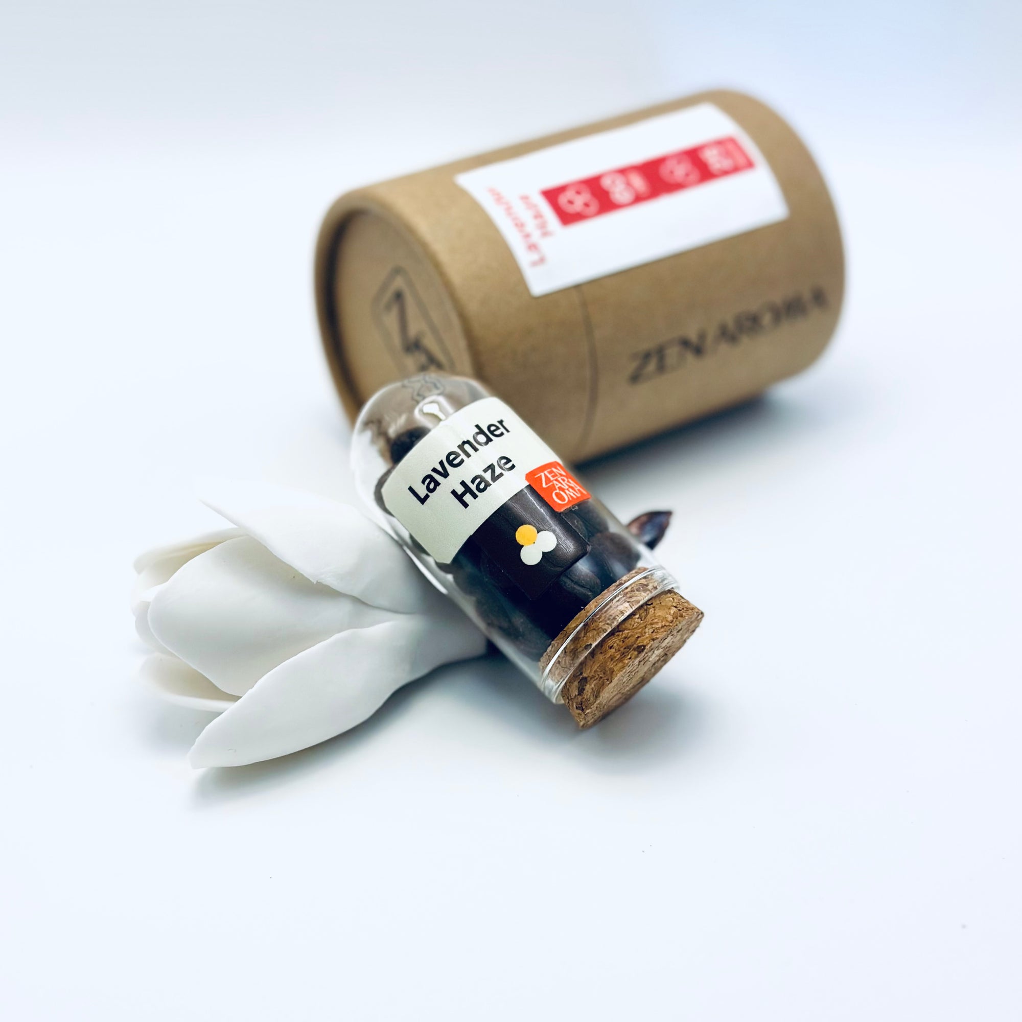 Zen Aroma Lavender Haze aroma pellets in a glass jar with cork lid, displayed with a kraft paper tube and white flower petals on a light background.