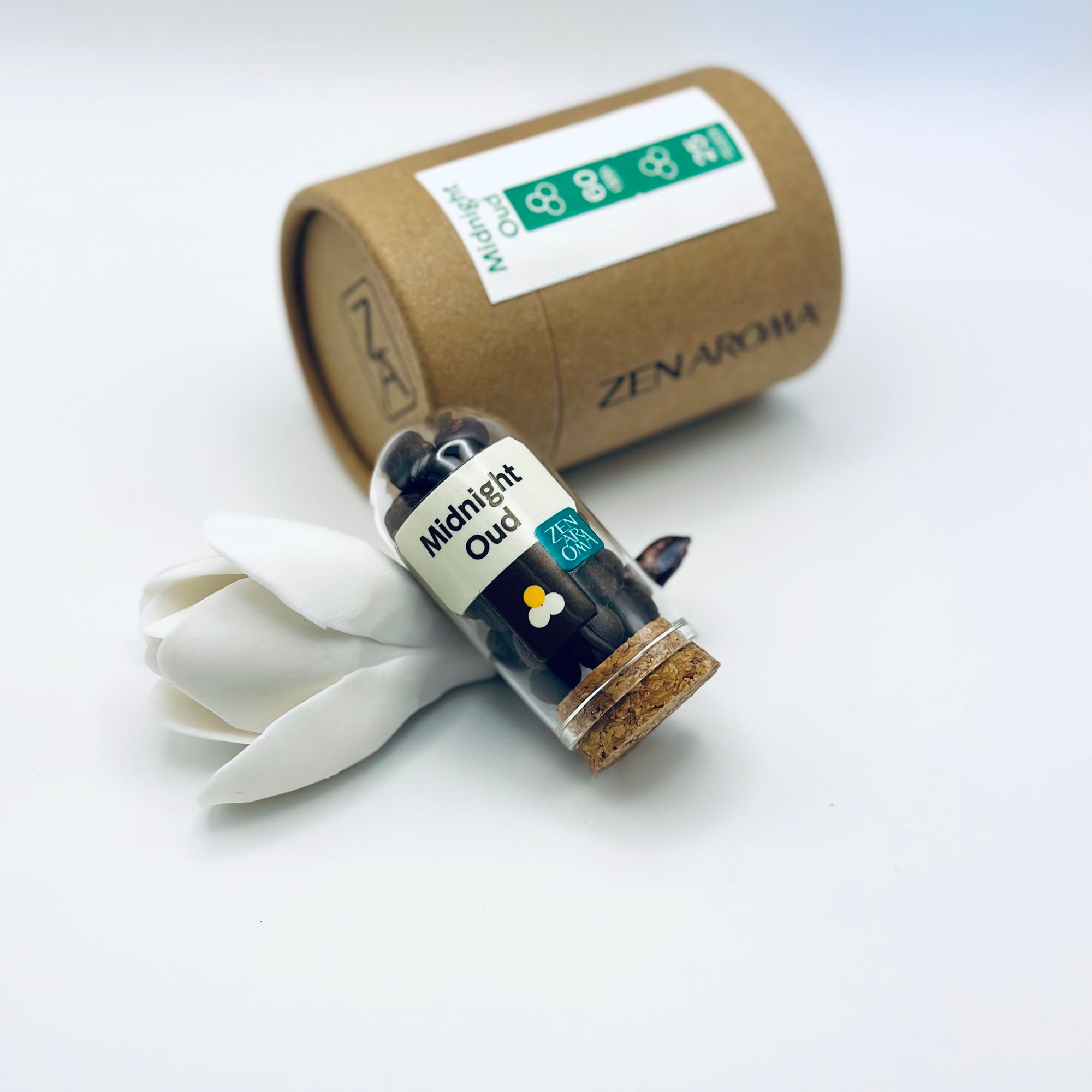 Zen Aroma Midnight Oud aroma pellets in a glass jar with cork lid, displayed with a kraft paper tube and white flower petals on a light background.