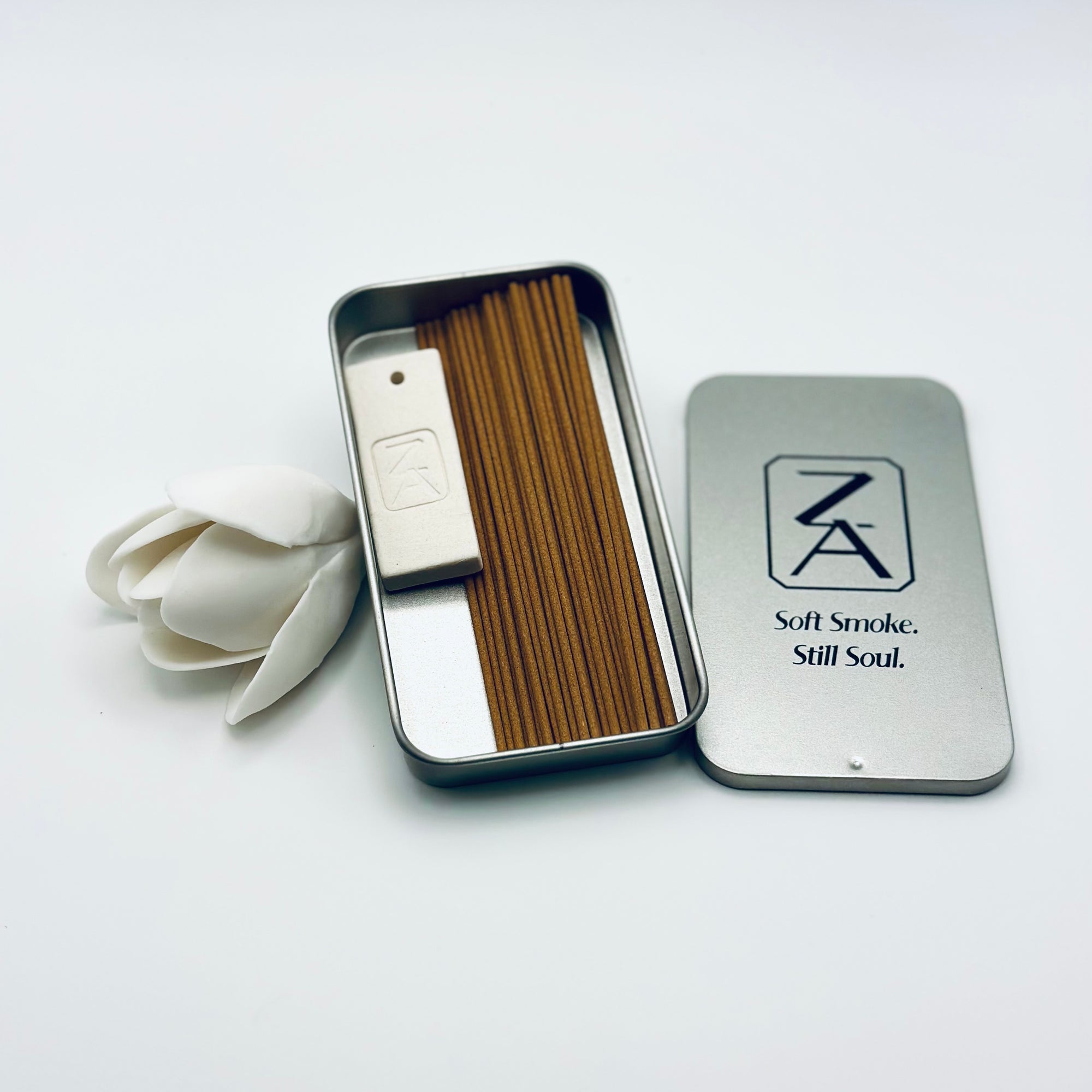 Zen Aroma To-Go Incense Kit featuring incense sticks, a minimalist ZA logo holder, and a metal case with “Soft Smoke. Still Soul.” branding beside a white flower.