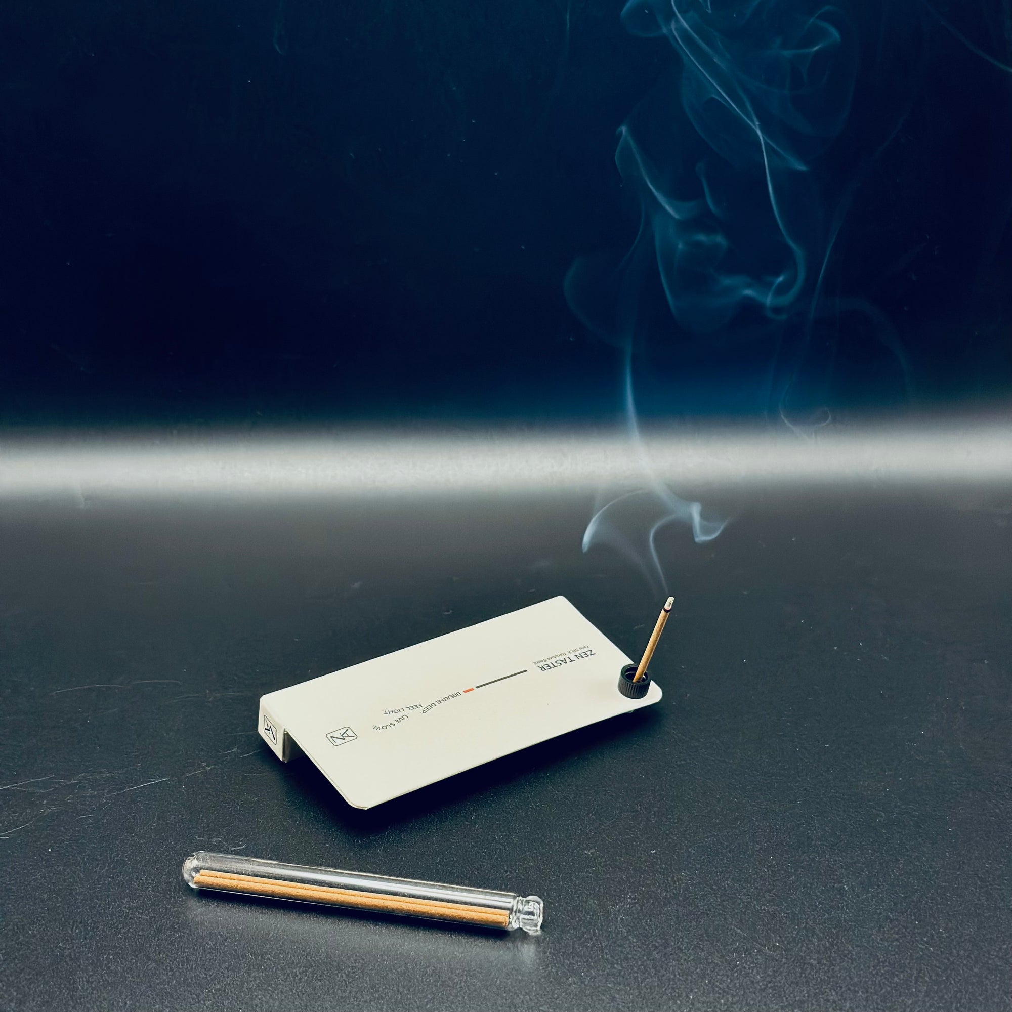 Zen Aroma “Zen Taster – Random Scent Trial” in use, showing incense stick burning with gentle smoke against a dark background, beside a glass incense tube.