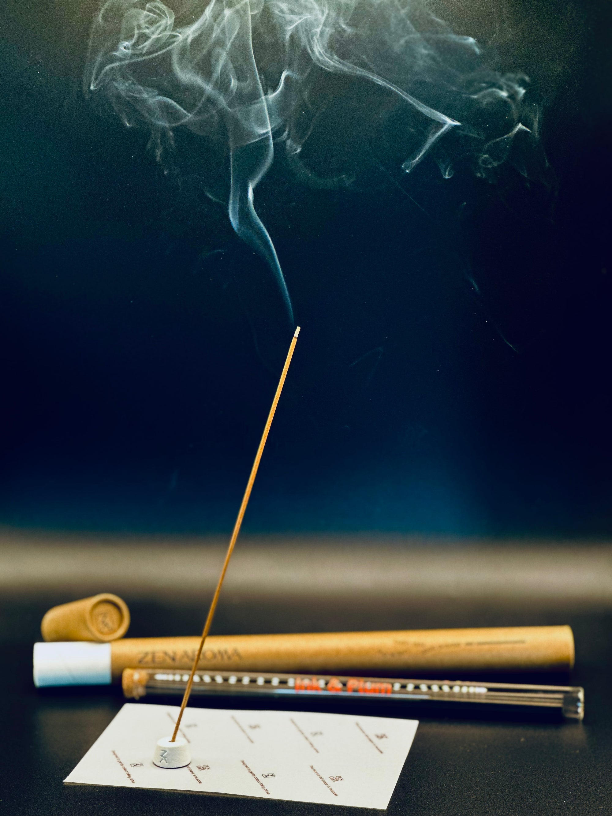 Lit Zen Aroma incense stick releasing gentle smoke, displayed with glass and cardboard packaging on a dark background — a serene and elegant home fragrance scene.